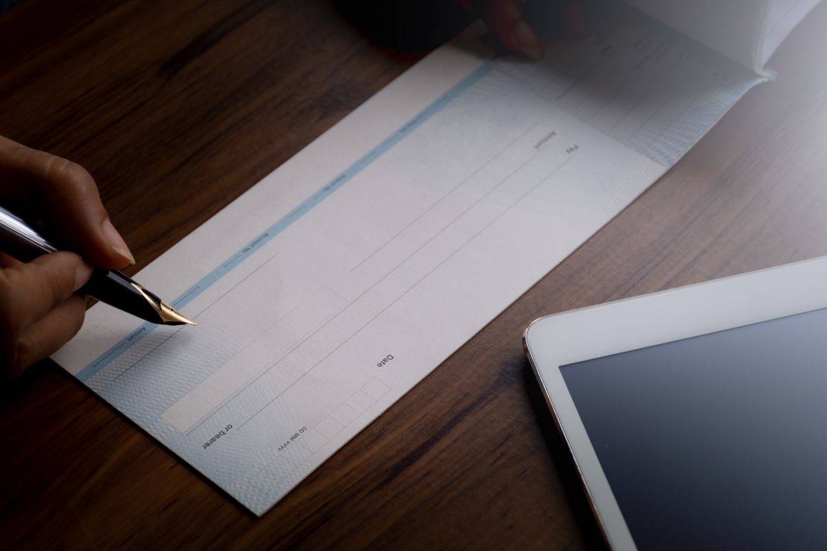 Woman hand holding pen and writing checkbook with digital tablet on wooden background. Business plan concept.